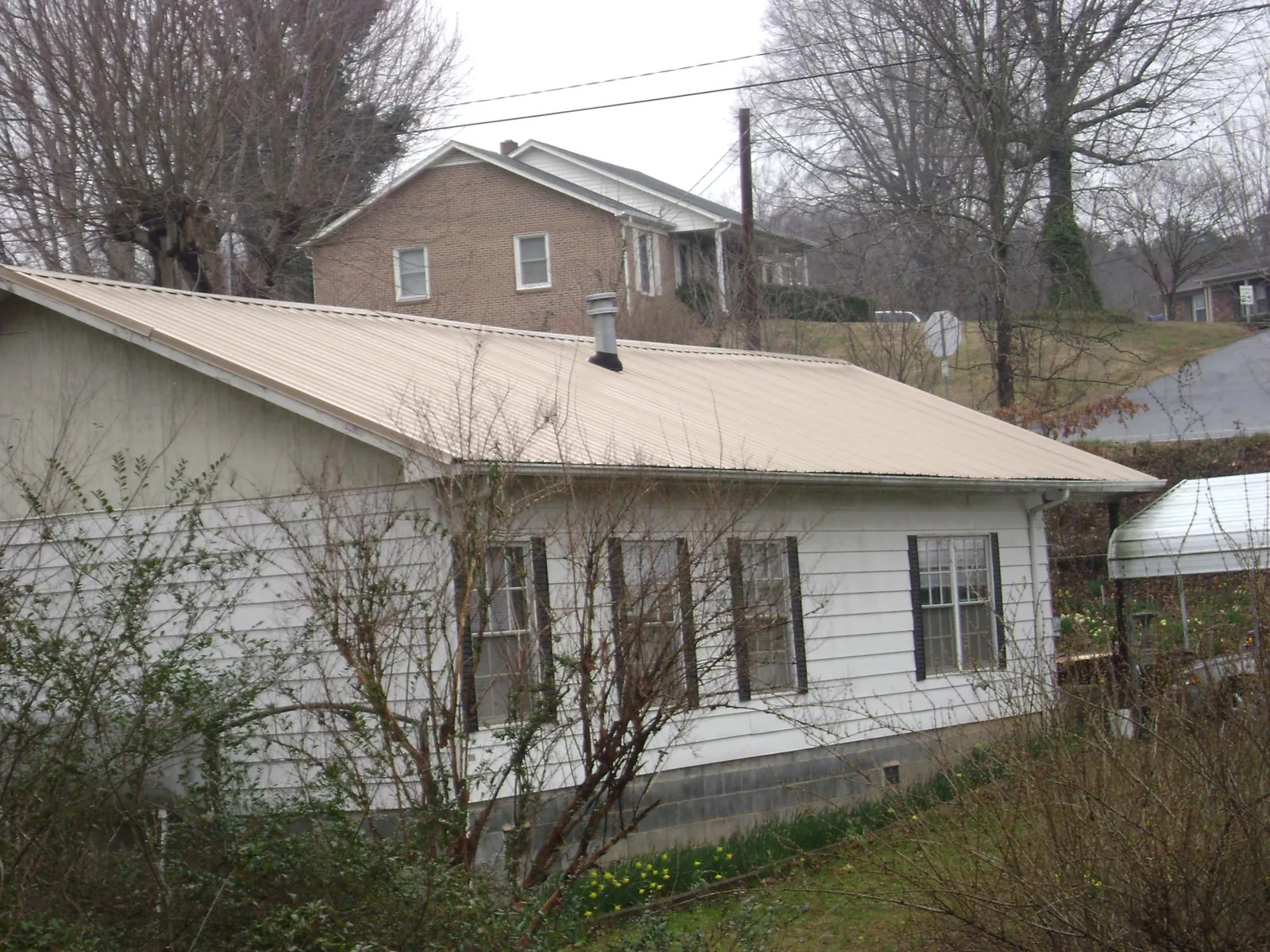 Tan metal roof on a white sided house set into a hillside — Commercial Roofing by Roofing Brothers in Livingston